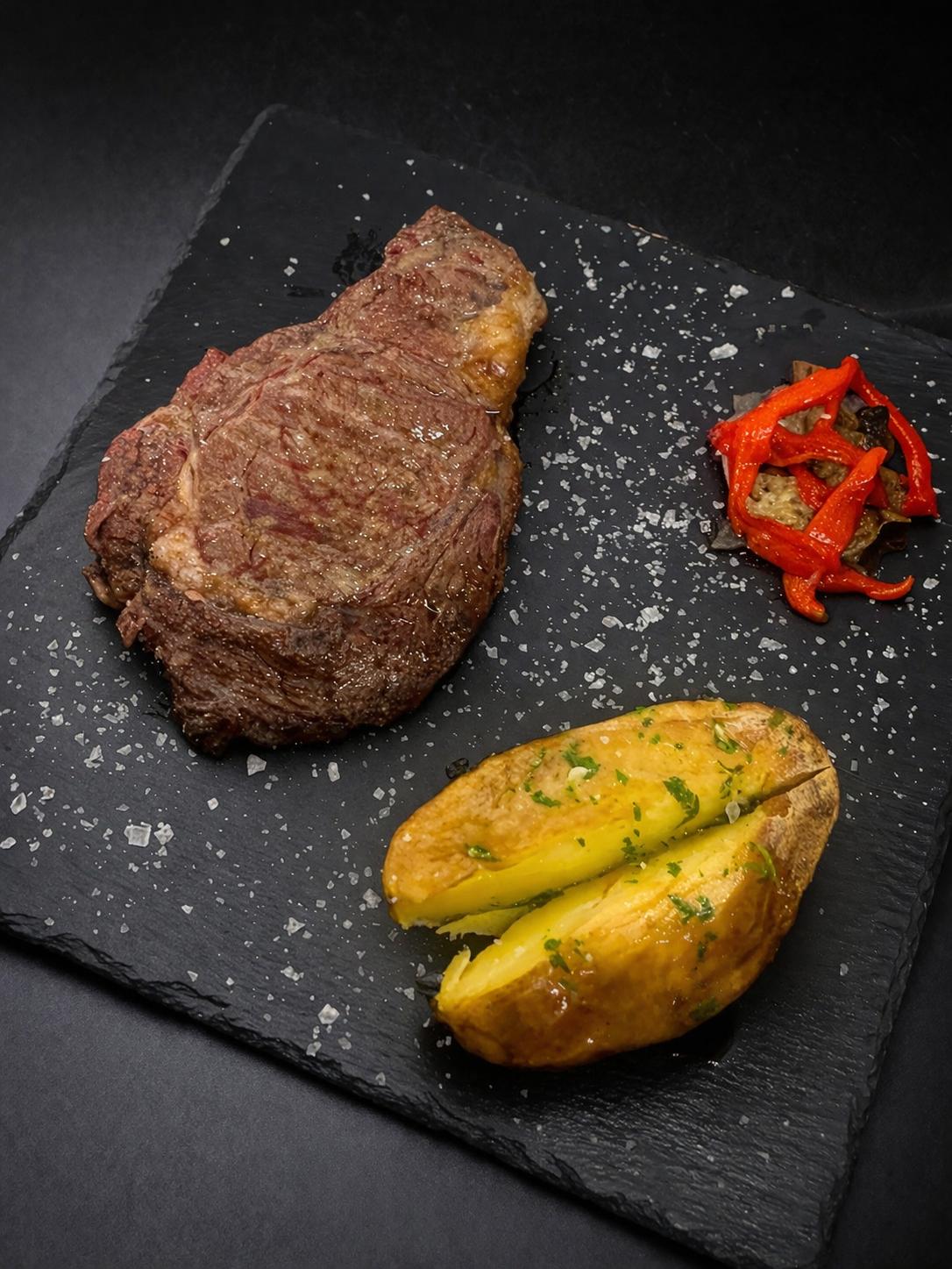 Entrecot a la brasa con patata y pimientos sobre pizarra negra